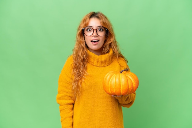 Young caucasian woman holding a pumpkin isolated on green screen chroma key background with surprise facial expression