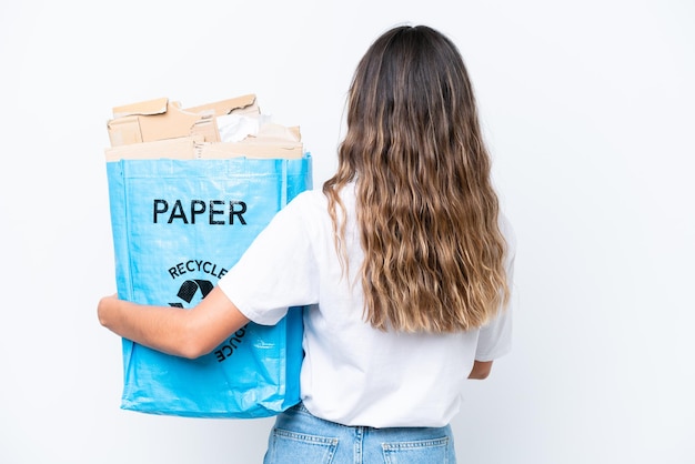 Young caucasian woman holding a recycling bag full of paper to recycle isolated on white background in back position