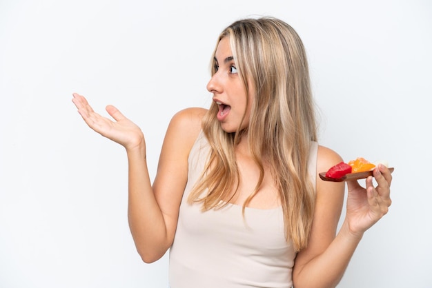 Young caucasian woman holding sashimi isolated on white background with surprise facial expression