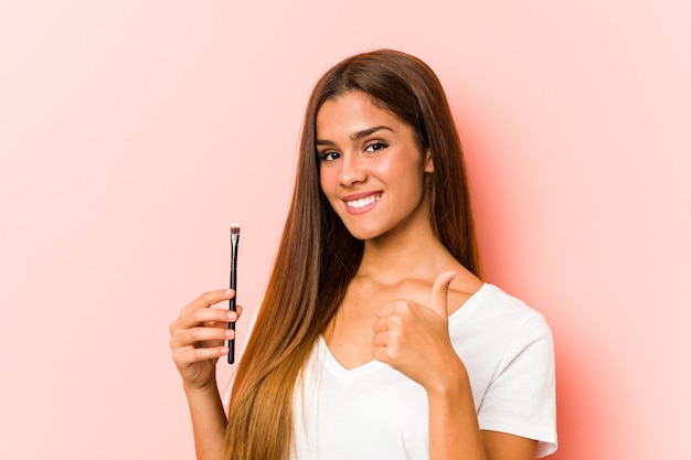 Young caucasian woman holding an skinbrush smiling and raising thumb up