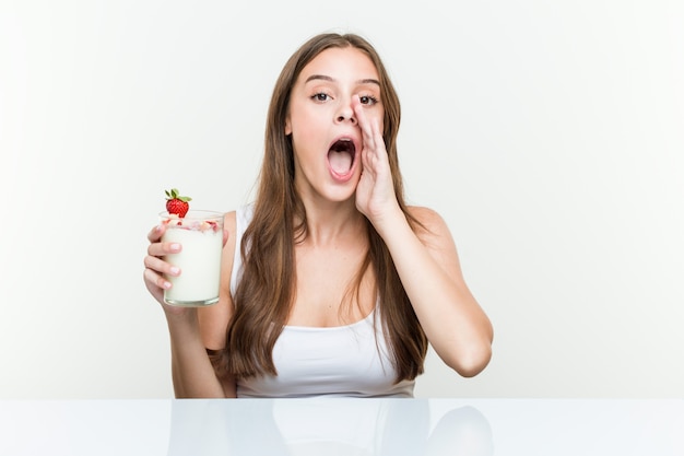 Young caucasian woman holding a smoothie shouting excited to front.