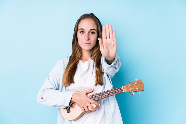 Young caucasian woman holding a ukelele standing with outstretched hand showing stop sign