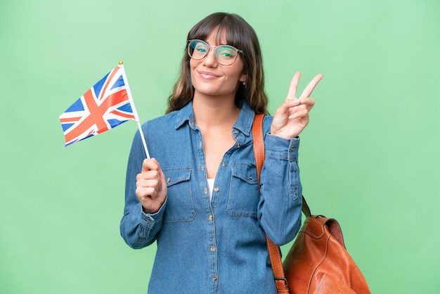 Young caucasian woman holding an United Kingdom flag over isolated background smiling and showing victory sign