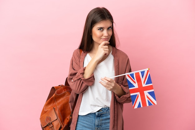 Young caucasian woman holding an United Kingdom flag isolated looking to the side and smiling