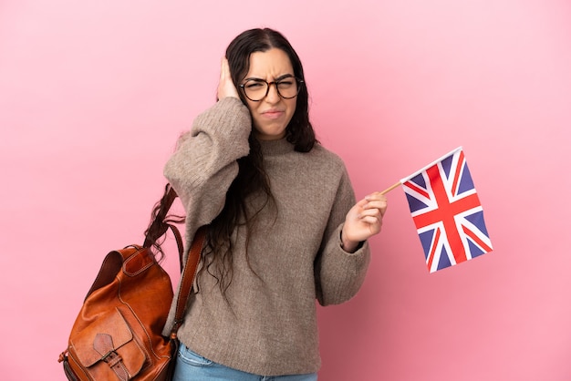 Young caucasian woman holding an United Kingdom flag isolated on pink wall frustrated and covering ears