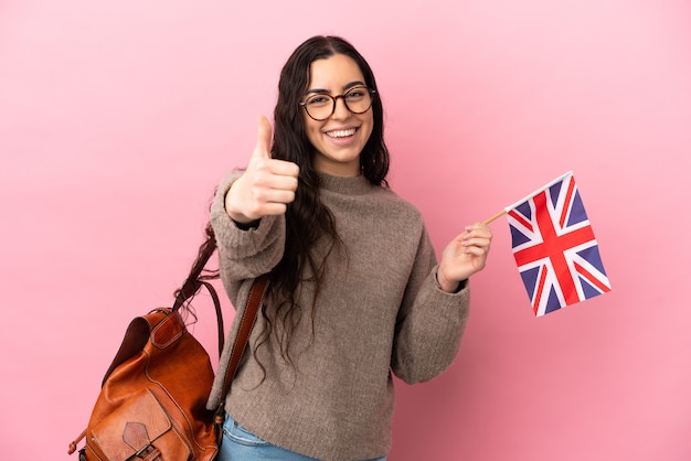 Young caucasian woman holding an United Kingdom flag isolated on pink wall with thumbs up because something good has happened