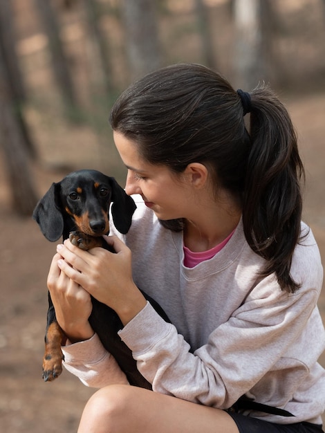 Young caucasian woman hugging black smooth haired miniature dachshund in forest