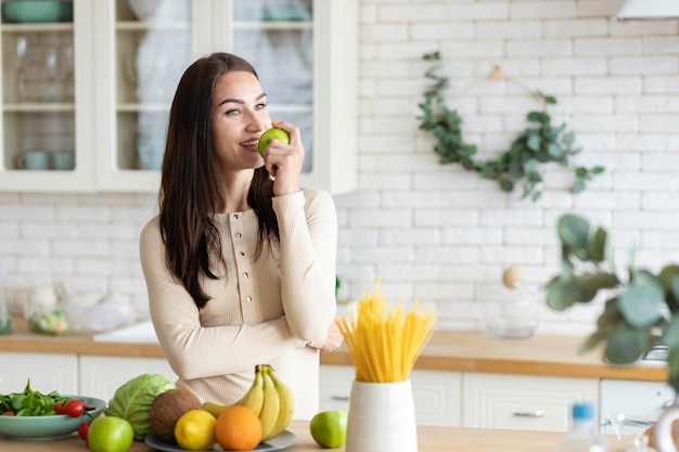 Young caucasian woman is standing in the kitchen with a green apple in her hands. Healthy lifestyle and healthy food concept