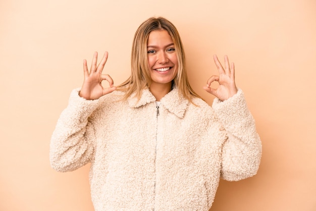 Young caucasian woman isolated on beige background cheerful and confident showing ok gesture.