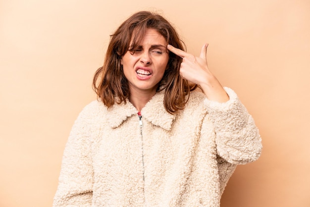 Young caucasian woman isolated on beige background covering ears with hands