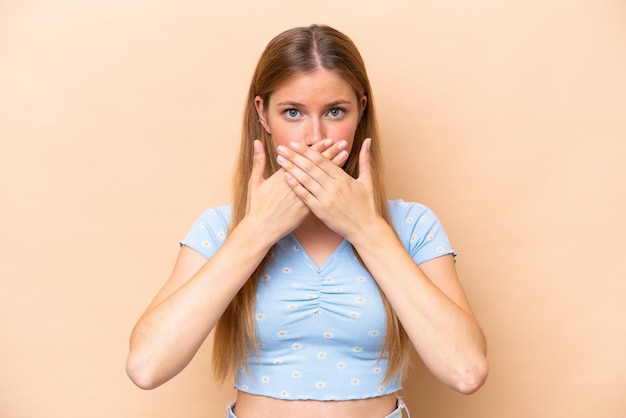 Young caucasian woman isolated on beige background covering mouth with hands