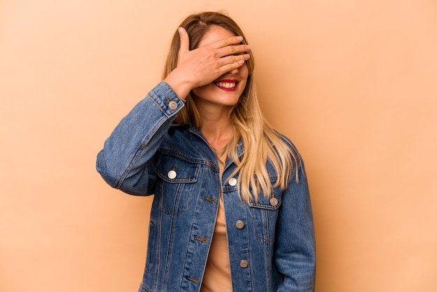 Young caucasian woman isolated on beige background covers eyes with hands smiles broadly waiting for a surprise