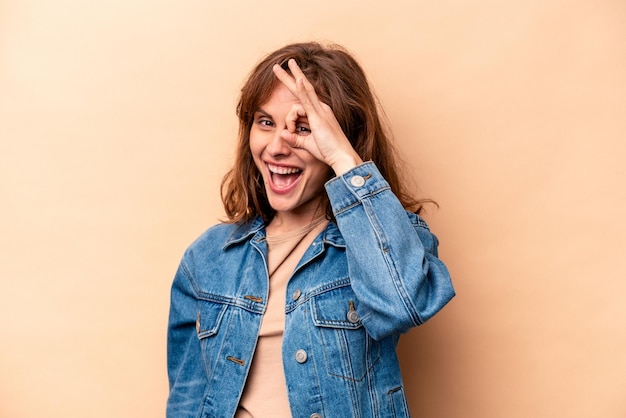 Young caucasian woman isolated on beige background excited keeping ok gesture on eye