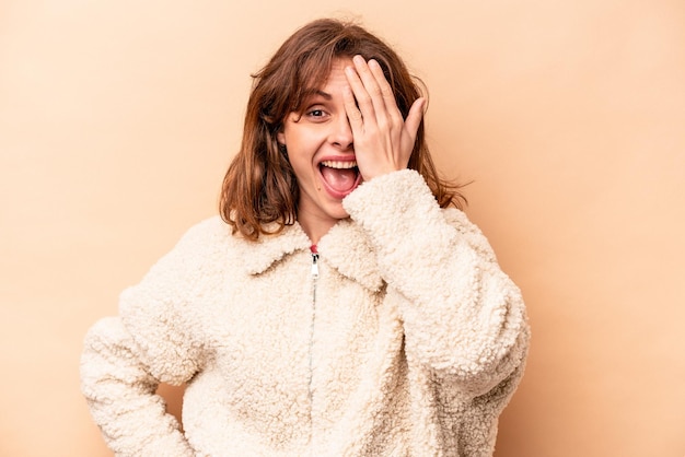 Young caucasian woman isolated on beige background having fun covering half of face with palm