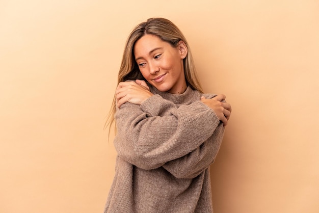 Young caucasian woman isolated on beige background hugs, smiling carefree and happy.