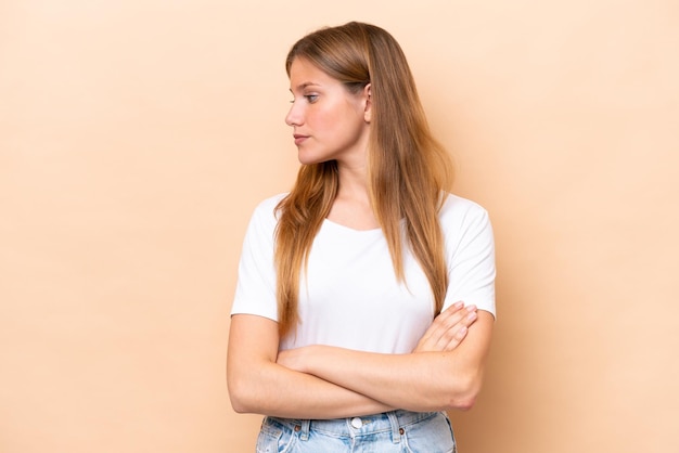 Young caucasian woman isolated on beige background keeping the arms crossed