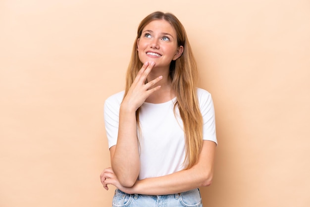 Young caucasian woman isolated on beige background looking up while smiling