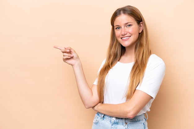 Young caucasian woman isolated on beige background pointing finger to the side