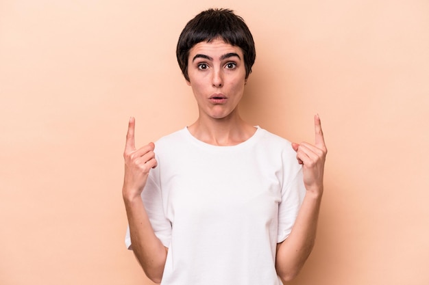 Young caucasian woman isolated on beige background pointing upside with opened mouth.