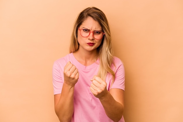 Young caucasian woman isolated on beige background showing fist to camera aggressive facial expression