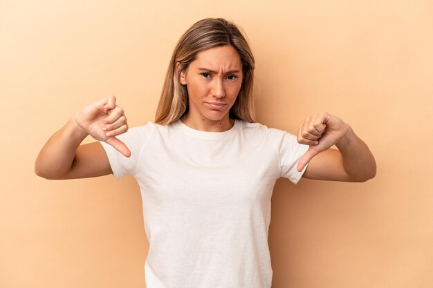 Young caucasian woman isolated on beige background showing thumb down, disappointment concept.