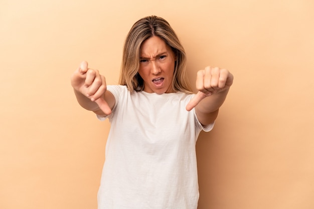 Young caucasian woman isolated on beige background showing thumb down and expressing dislike.