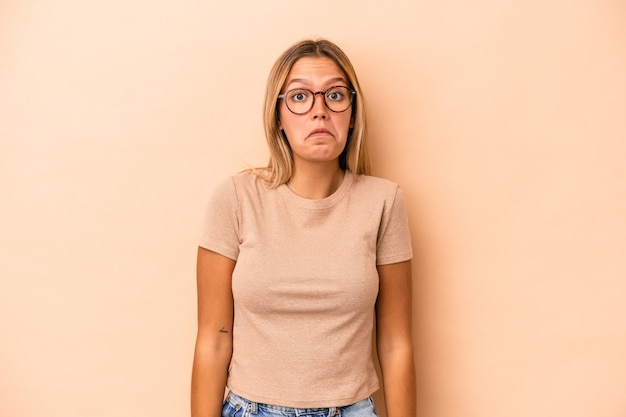 Young caucasian woman isolated on beige background shrugs shoulders and open eyes confused.