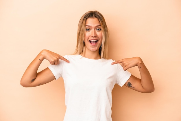 Young caucasian woman isolated on beige background surprised pointing with finger, smiling broadly.