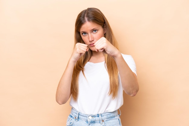 Young caucasian woman isolated on beige background with fighting gesture