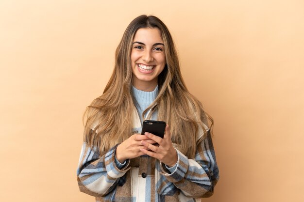 Young caucasian woman isolated on beige wall sending a message with the mobile