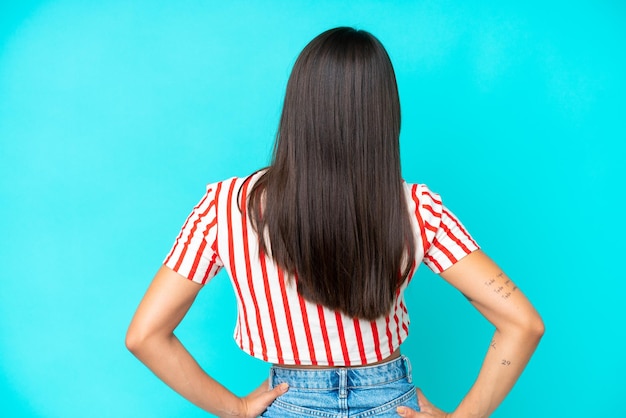 Young caucasian woman isolated on blue background in back position