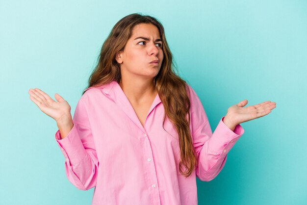 Young caucasian woman isolated on blue background  confused and doubtful shrugging shoulders to hold a copy space.