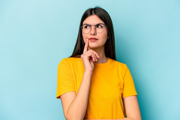 Young caucasian woman isolated on blue background contemplating planning a strategy thinking about the way of a business