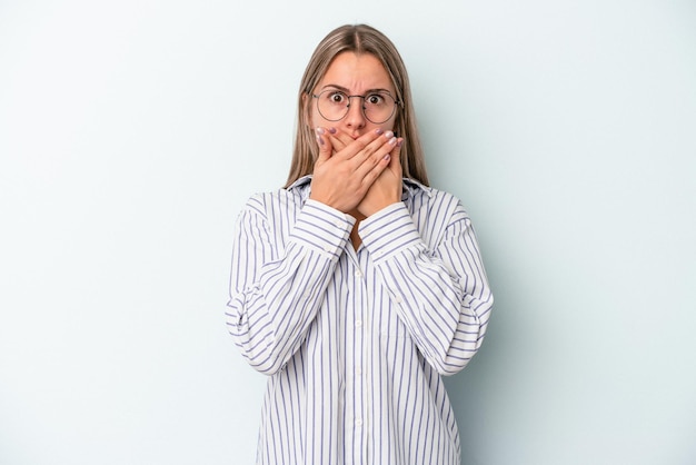 Young caucasian woman isolated on blue background covering mouth with hands looking worried.