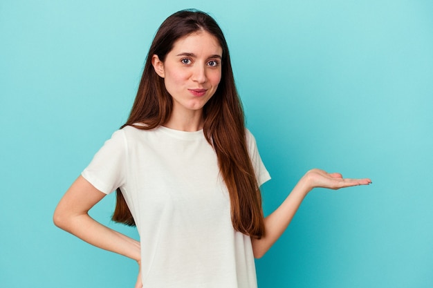 Young caucasian woman isolated on blue background doubting and shrugging shoulders in questioning gesture.