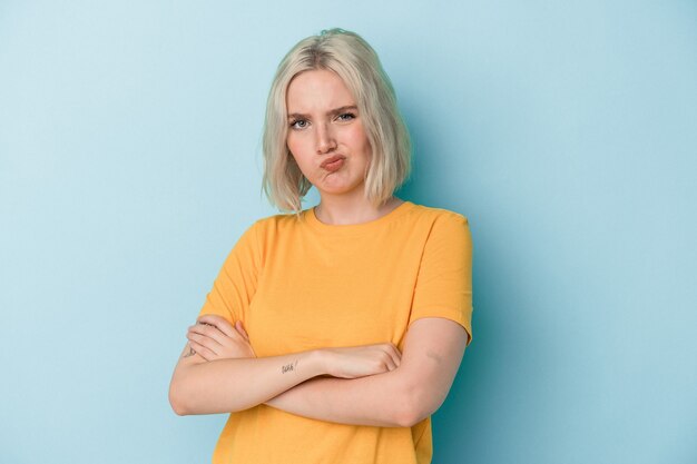 Young caucasian woman isolated on blue background frowning face in displeasure, keeps arms folded.