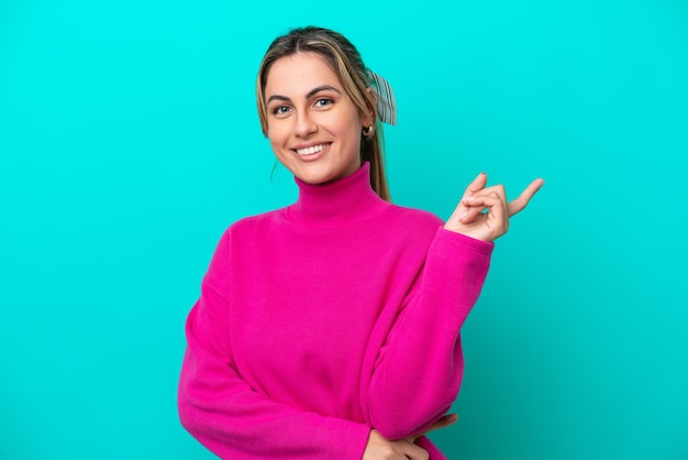 Young caucasian woman isolated on blue background happy and pointing up