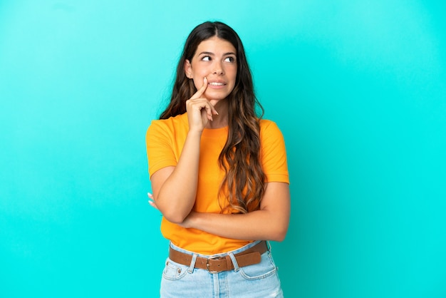 Young caucasian woman isolated on blue background having doubts while looking up