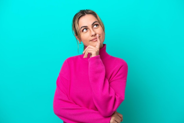 Young caucasian woman isolated on blue background having doubts while looking up