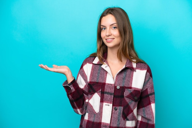 Young caucasian woman isolated on blue background holding copyspace imaginary on the palm to insert an ad