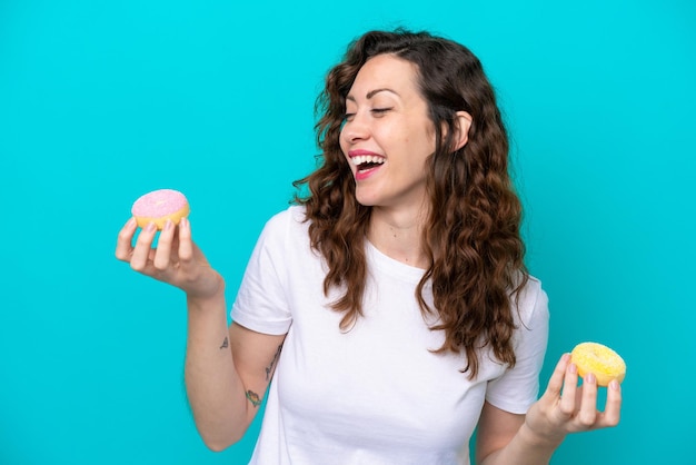 Young caucasian woman isolated on blue background holding donuts with happy expression