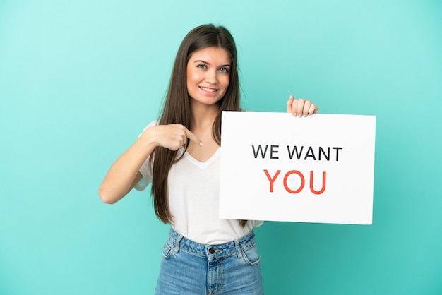 Young caucasian woman isolated on blue background holding We Want You board and  pointing it