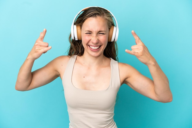 Young caucasian woman isolated on blue background listening music making rock gesture