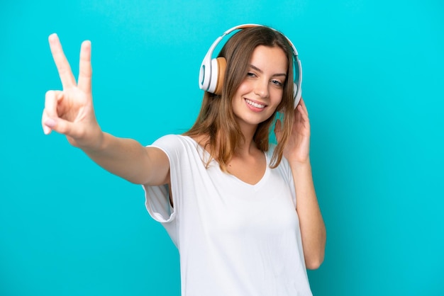 Young caucasian woman isolated on blue background listening music and singing