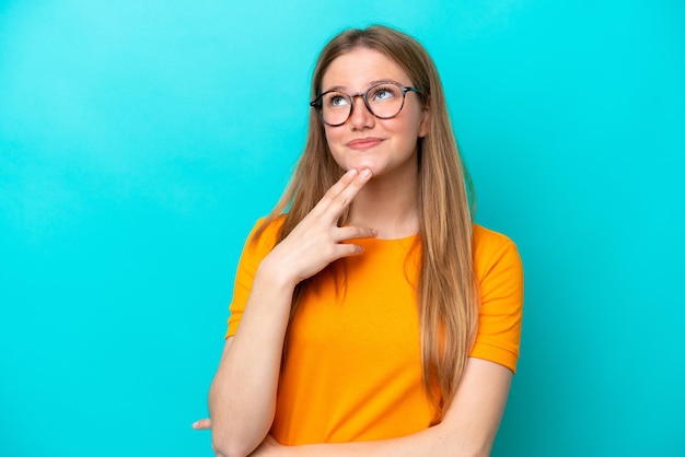 Young caucasian woman isolated on blue background looking up while smiling