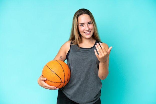 Young caucasian woman isolated on blue background playing basketball and doing coming gesture