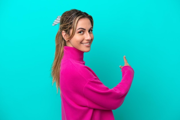 Young caucasian woman isolated on blue background pointing back