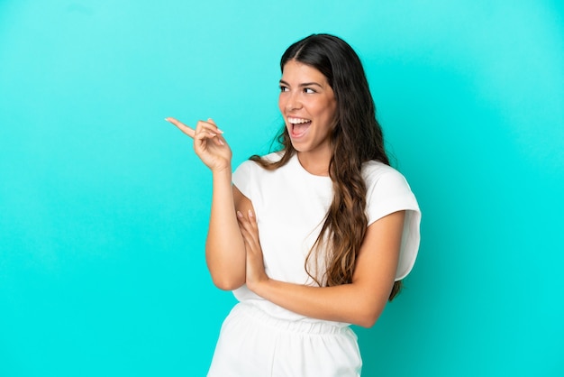 Young caucasian woman isolated on blue background pointing finger to the side and presenting a product