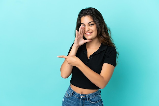 Young caucasian woman isolated on blue background pointing to the side to present a product and whispering something