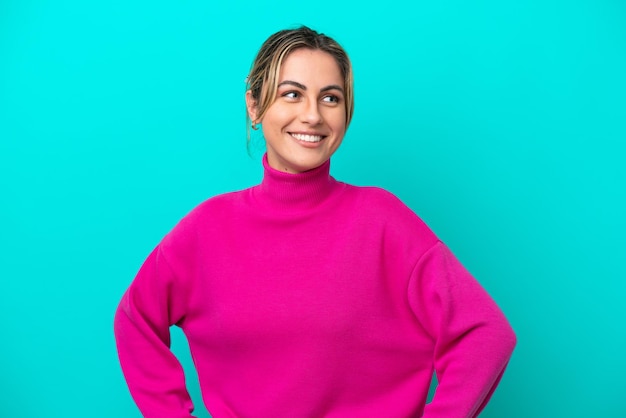 Young caucasian woman isolated on blue background posing with arms at hip and smiling